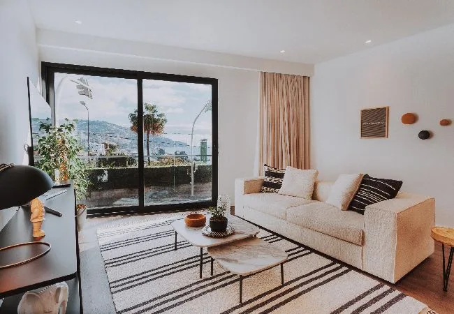 Una sala luminosa con un sofá junto a grandes ventanales con vistas al agua.