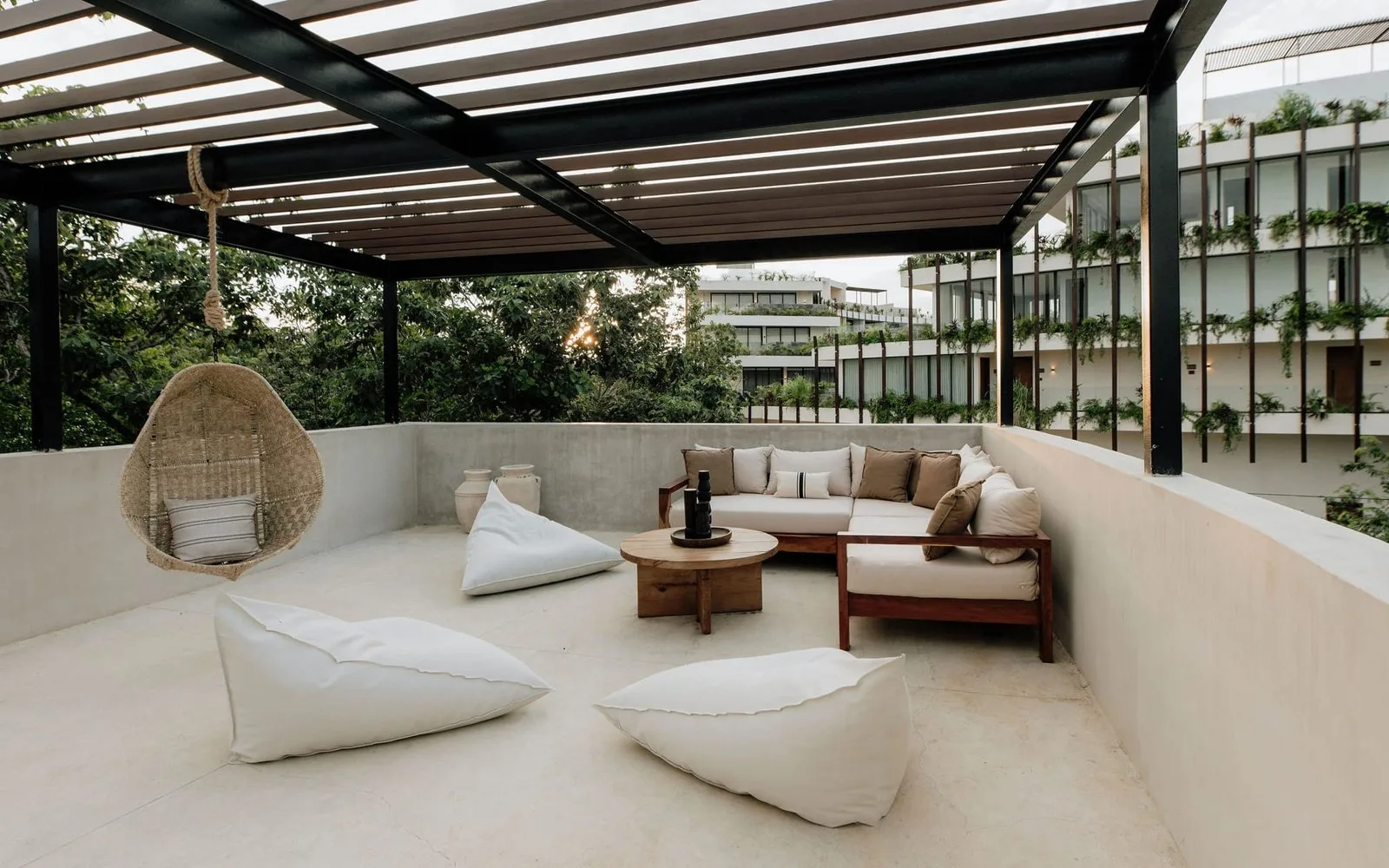 Una sala exterior cubierta tiene asientos bajos y una silla colgante de mimbre.