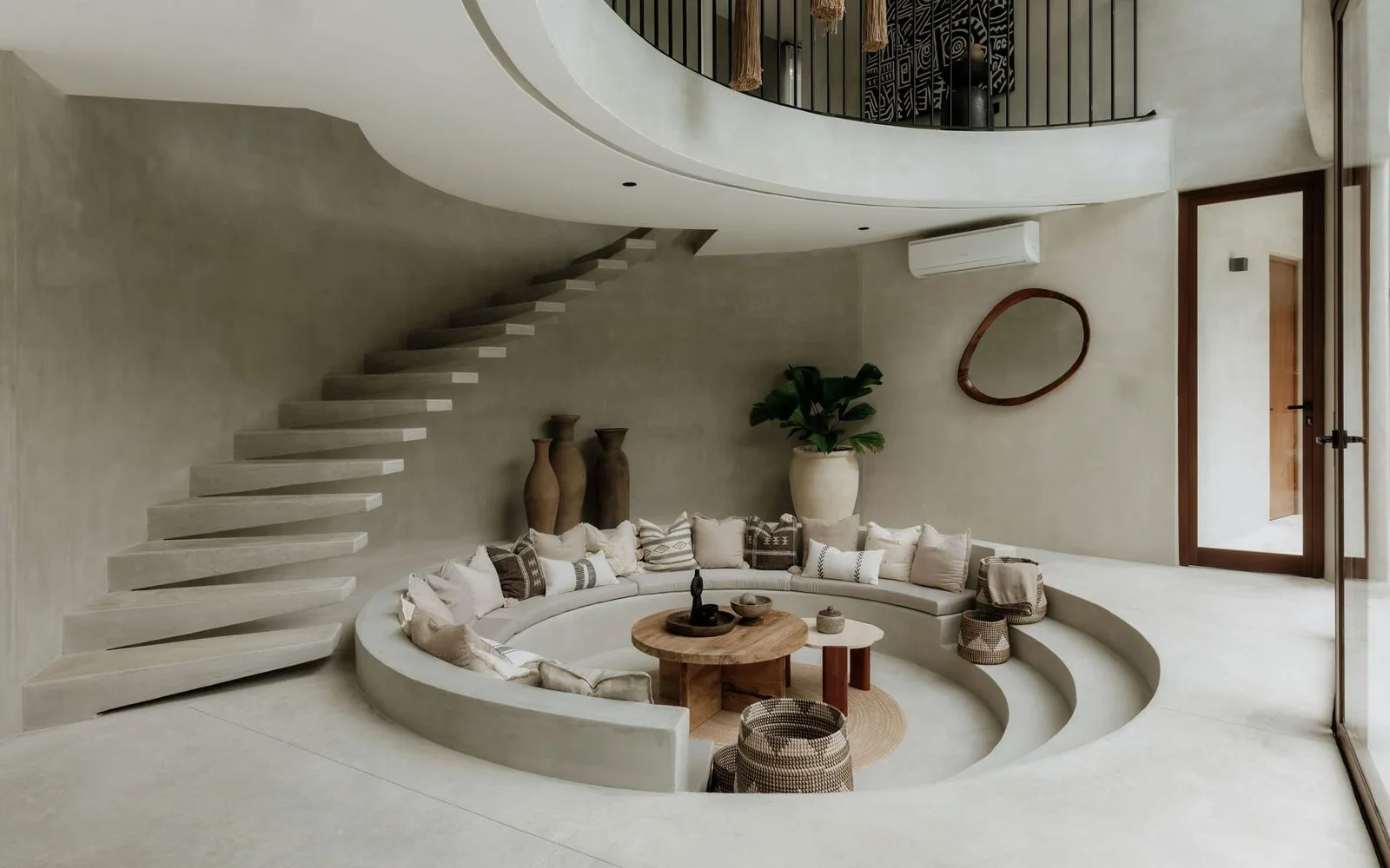 A sunken circular seating area sits beneath a curved staircase.