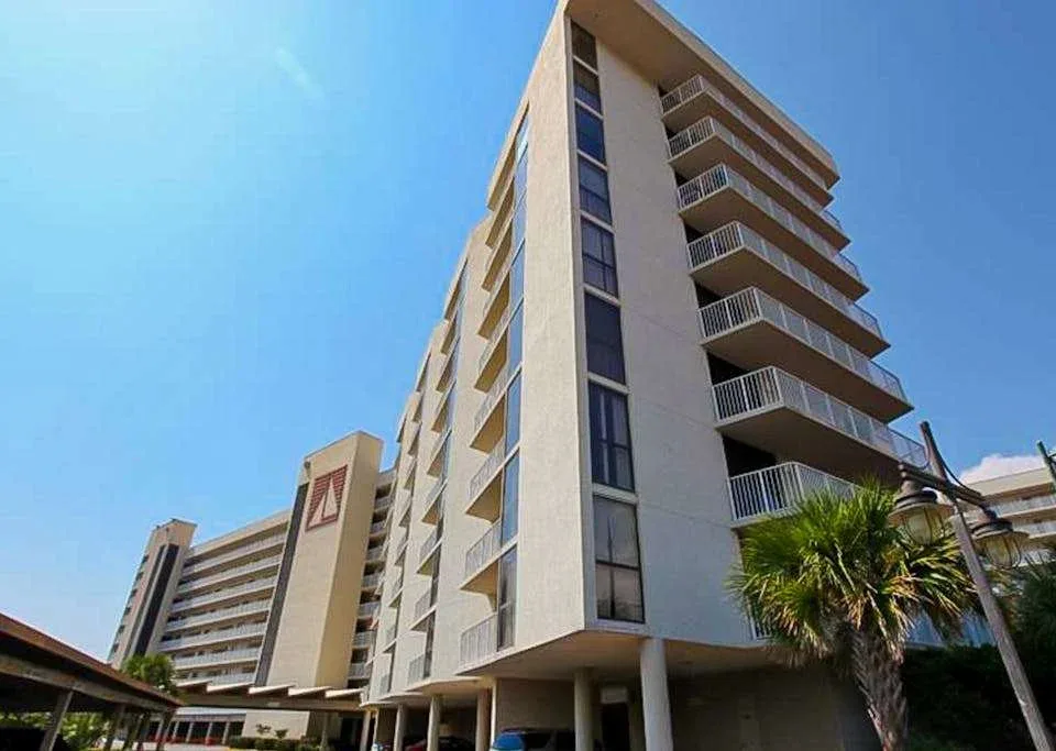 Zona común: Un edificio alto de apartamentos con balcones se alza bajo un cielo azul despejado.