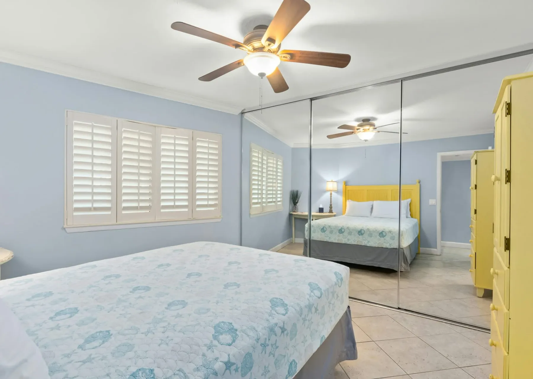 Un dormitorio con una cama, ventanas con contraventanas y puertas de armario espejadas.