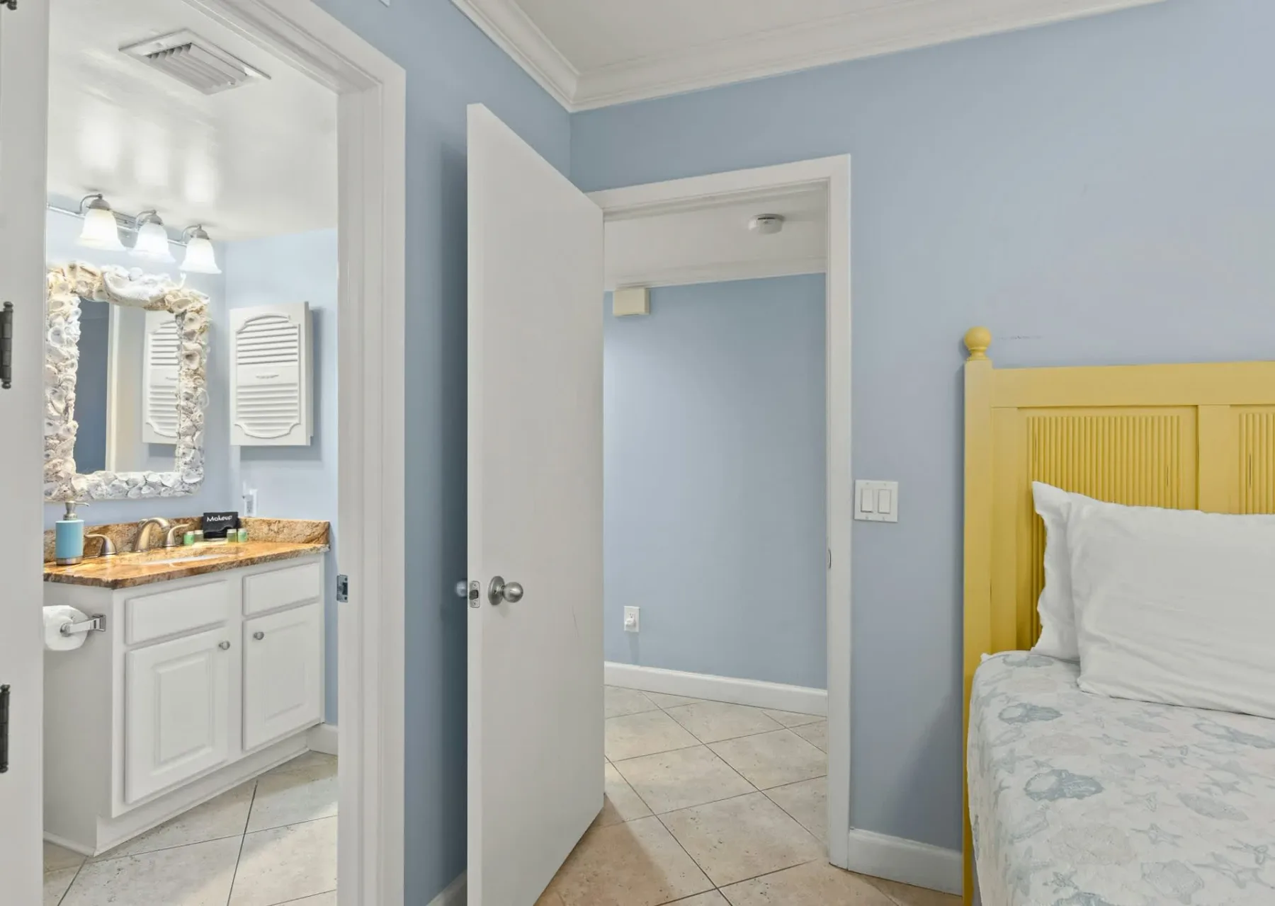 Un dormitorio con una cama de estructura amarilla junto a una puerta abierta hacia el baño.
