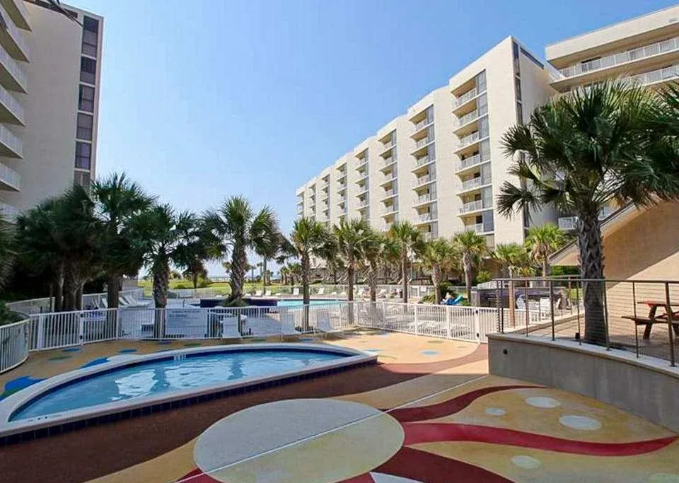 Zona común: Área de piscina al aire libre con pavimento de colores y palmeras.