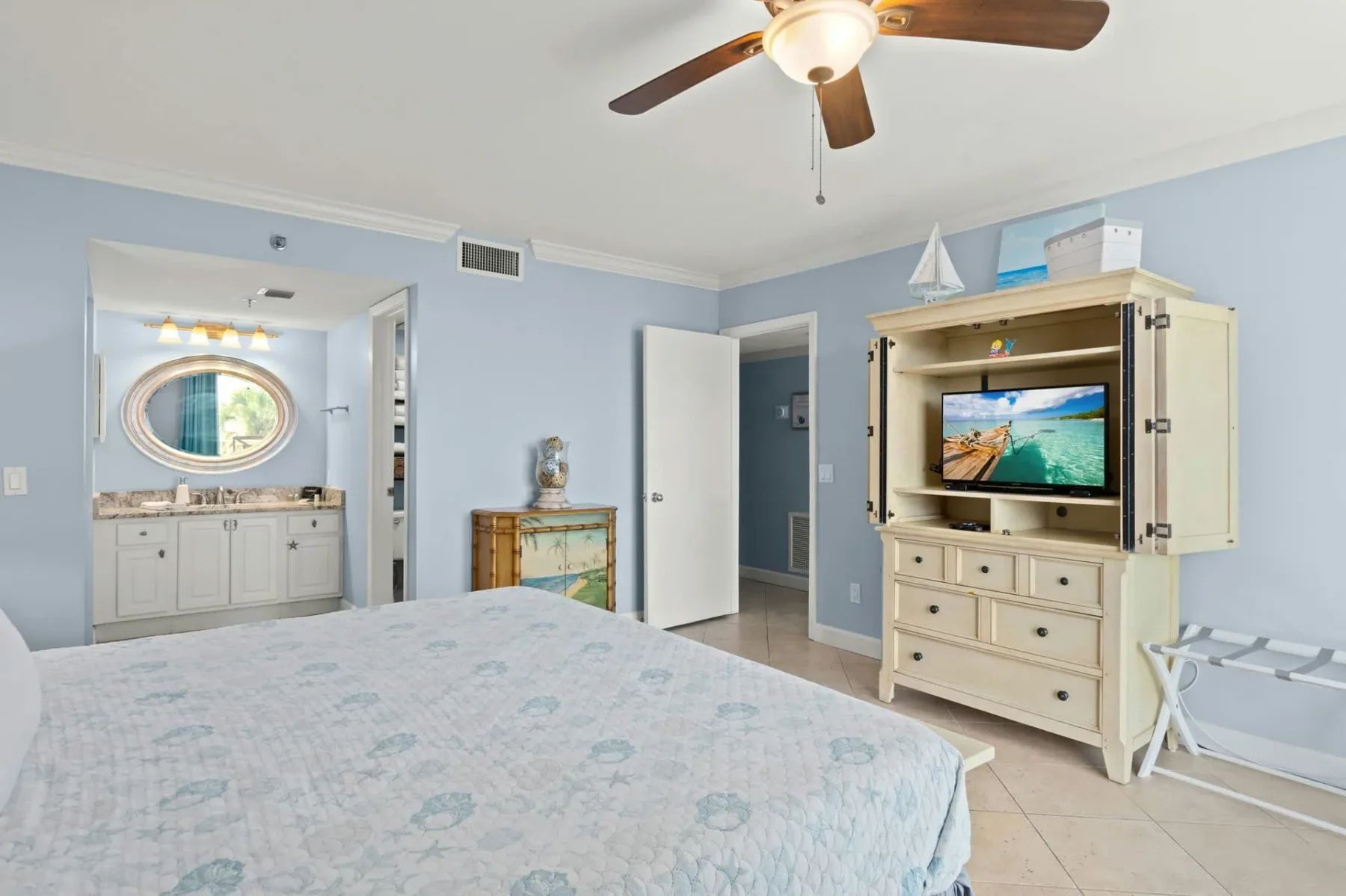 Un dormitorio con una cama, un ventilador de techo y un mueble para televisor.