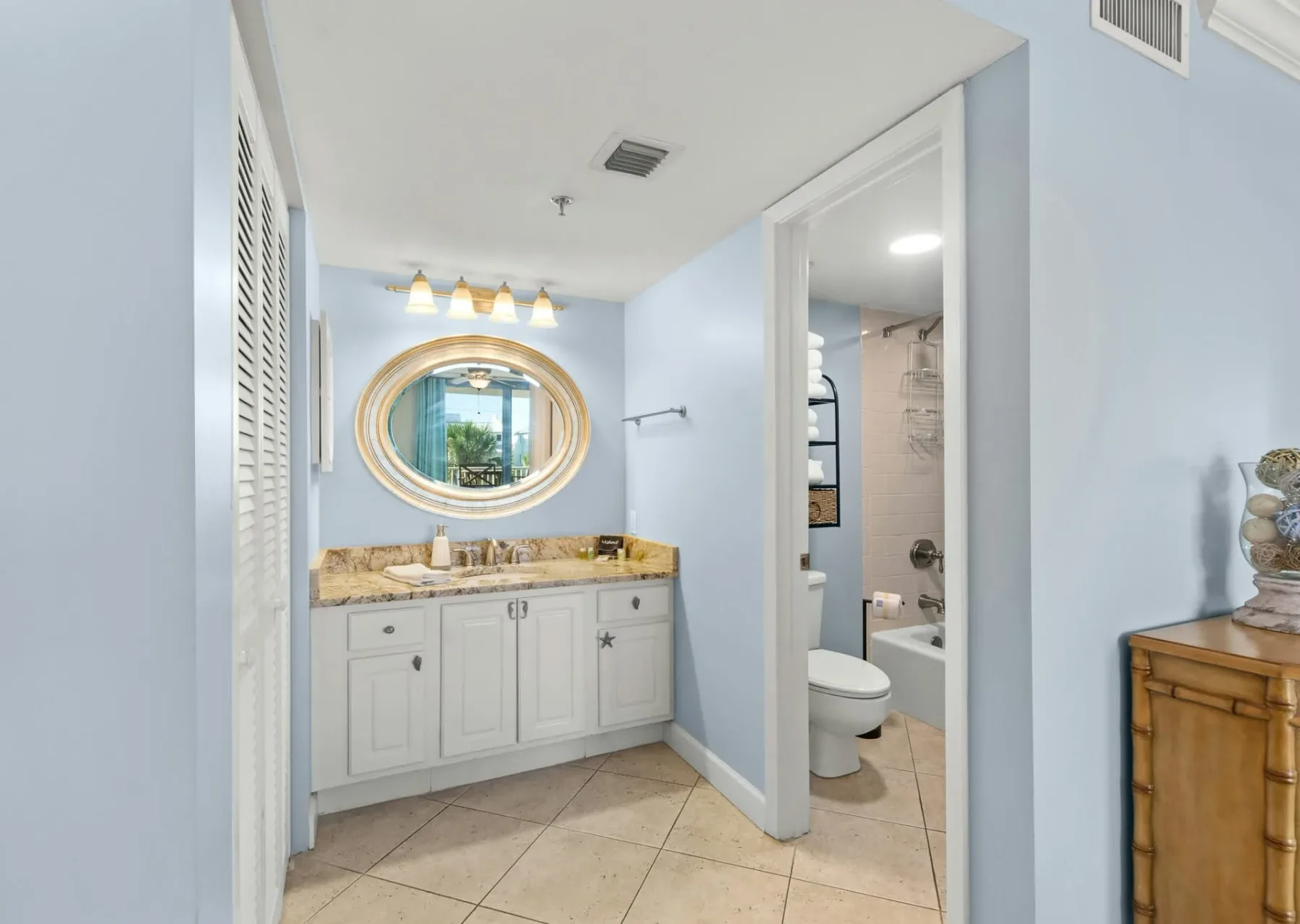 Un lavabo con espejo ovalado está junto a una puerta abierta que da al baño.