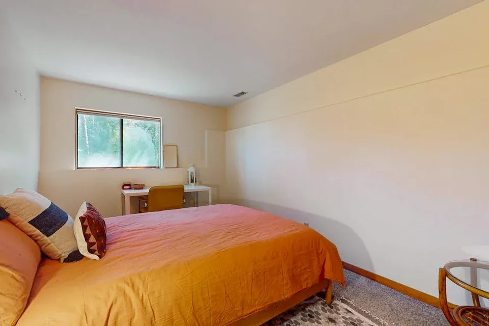 A bedroom with an orange bedspread and a window overlooking greenery.