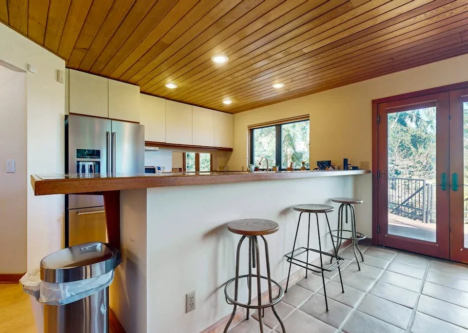 A kitchen with a long counter and bar stools beside glass doors.