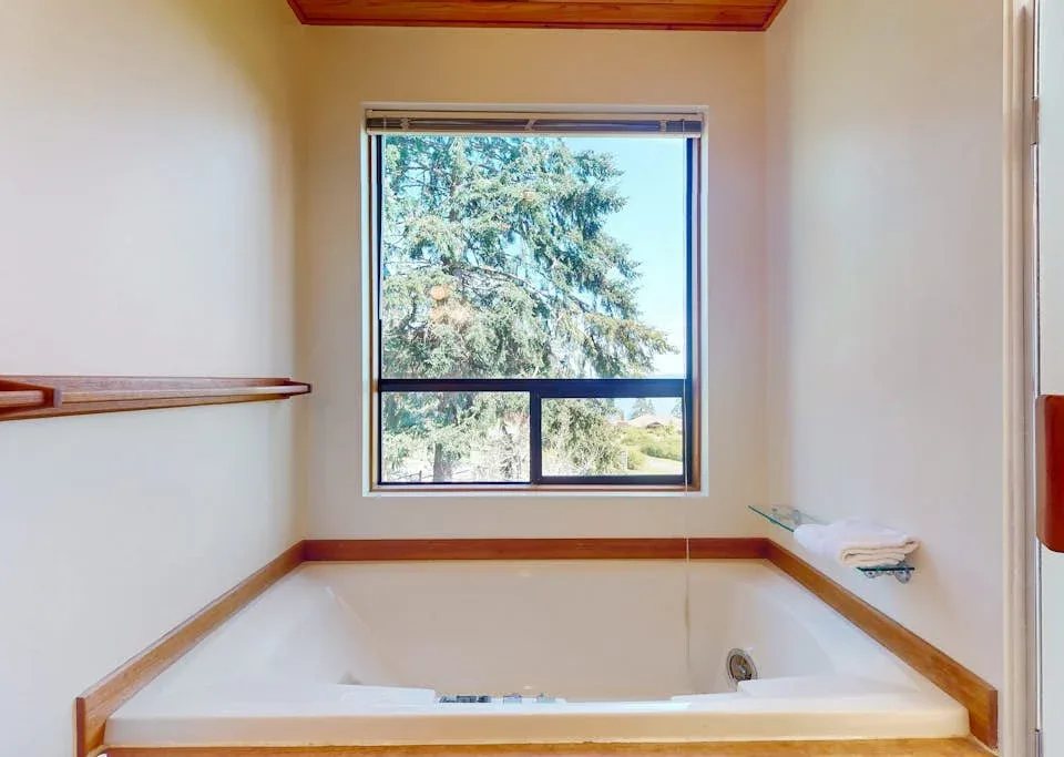 A bathroom with a built-in bathtub beneath a window overlooking trees.