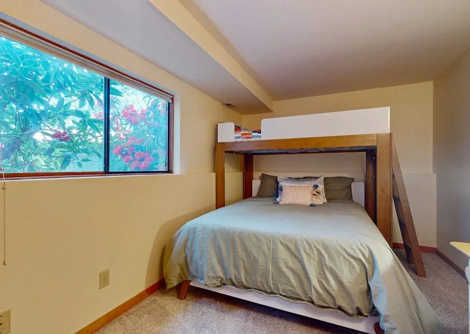 A bedroom with a bed beneath a wooden loft frame and a wide window.