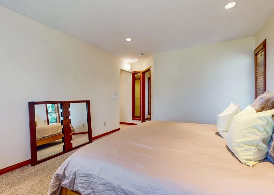 A bedroom with a bed, pillows, and a full-length mirror leaning against the wall.