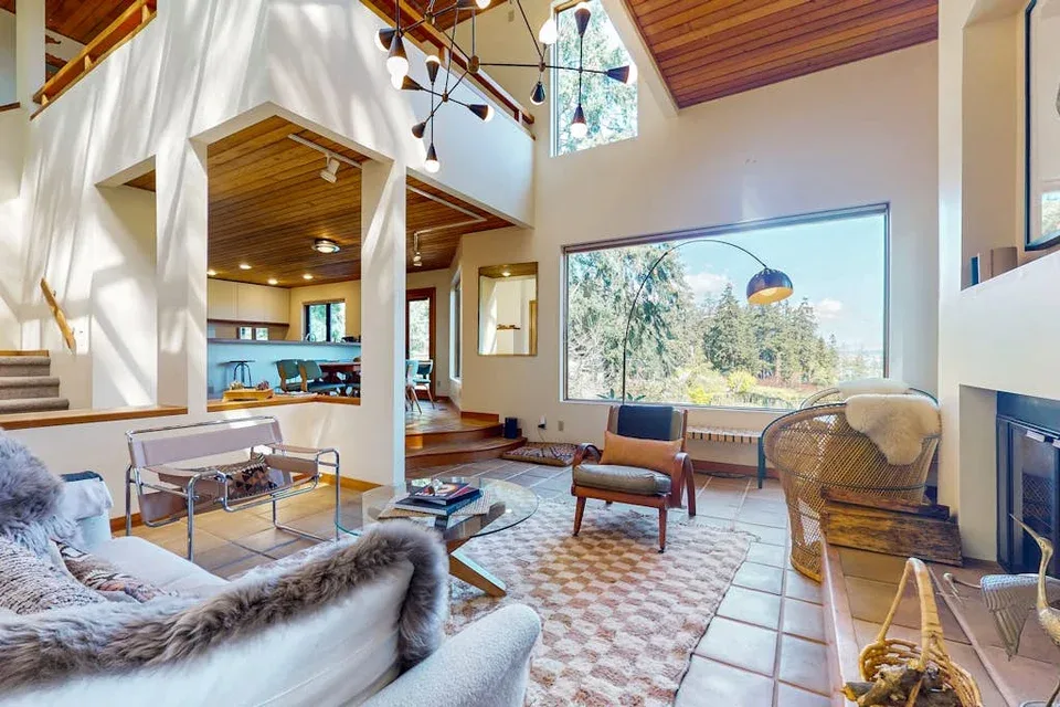 A bright living room with a large window, seating, and a fireplace.