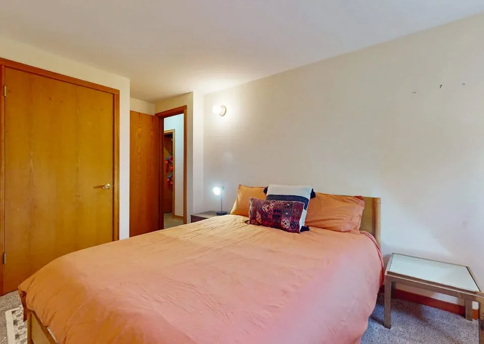 A bedroom with a large bed covered in pink bedding and a wooden door.