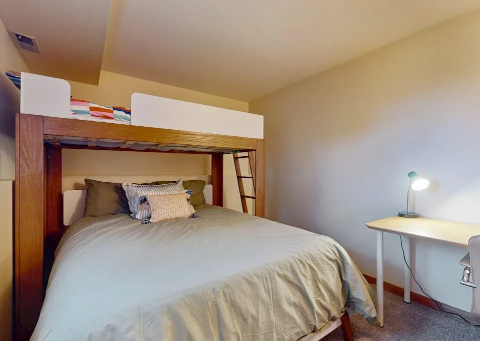 A bedroom with a double bed beneath a wooden loft bed and a desk lamp.