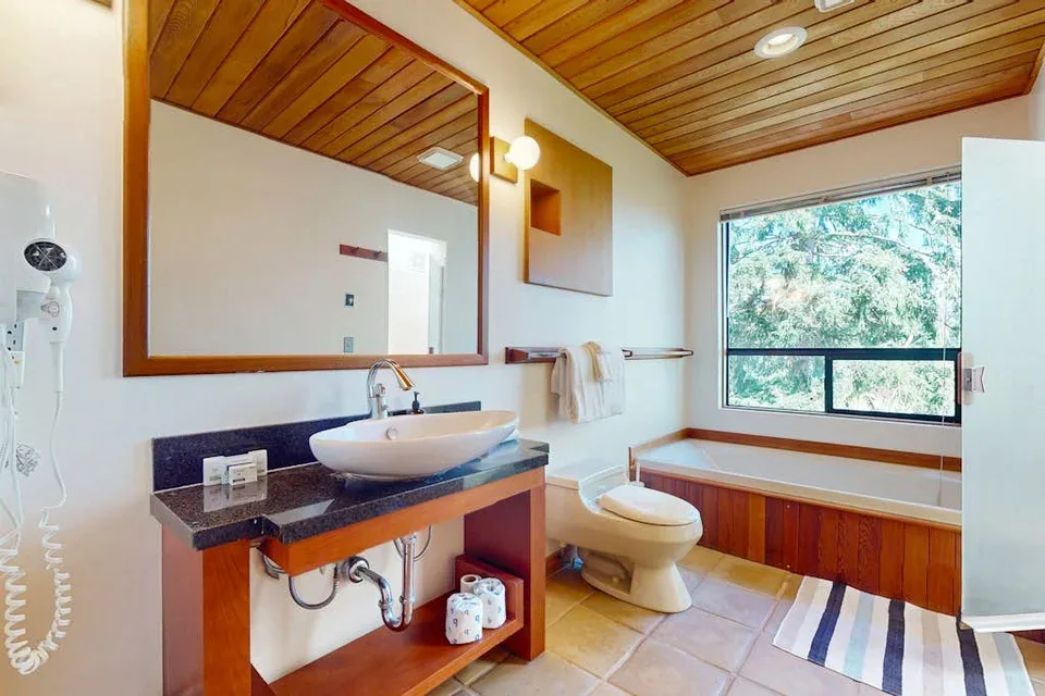 A bathroom with a sink, toilet, and bathtub beneath a large window.
