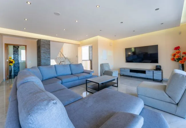 Una sala luminosa con asientos seccionales, una mesa de centro y un televisor en la pared.