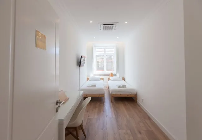 Un dormitorio luminoso con dos camas junto a una ventana.
