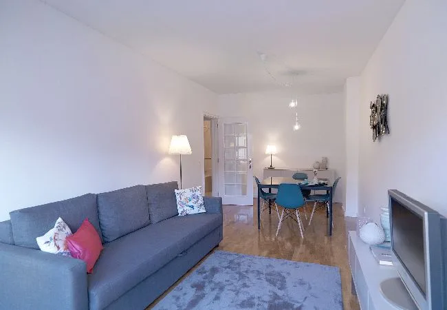 Una sala de estar con un sofá gris, una mesa de comedor y un televisor.