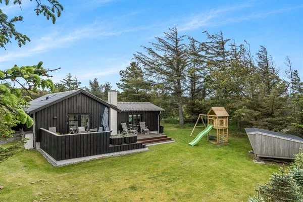 A dark wooden house sits beside a grassy yard with a play structure and slide.
