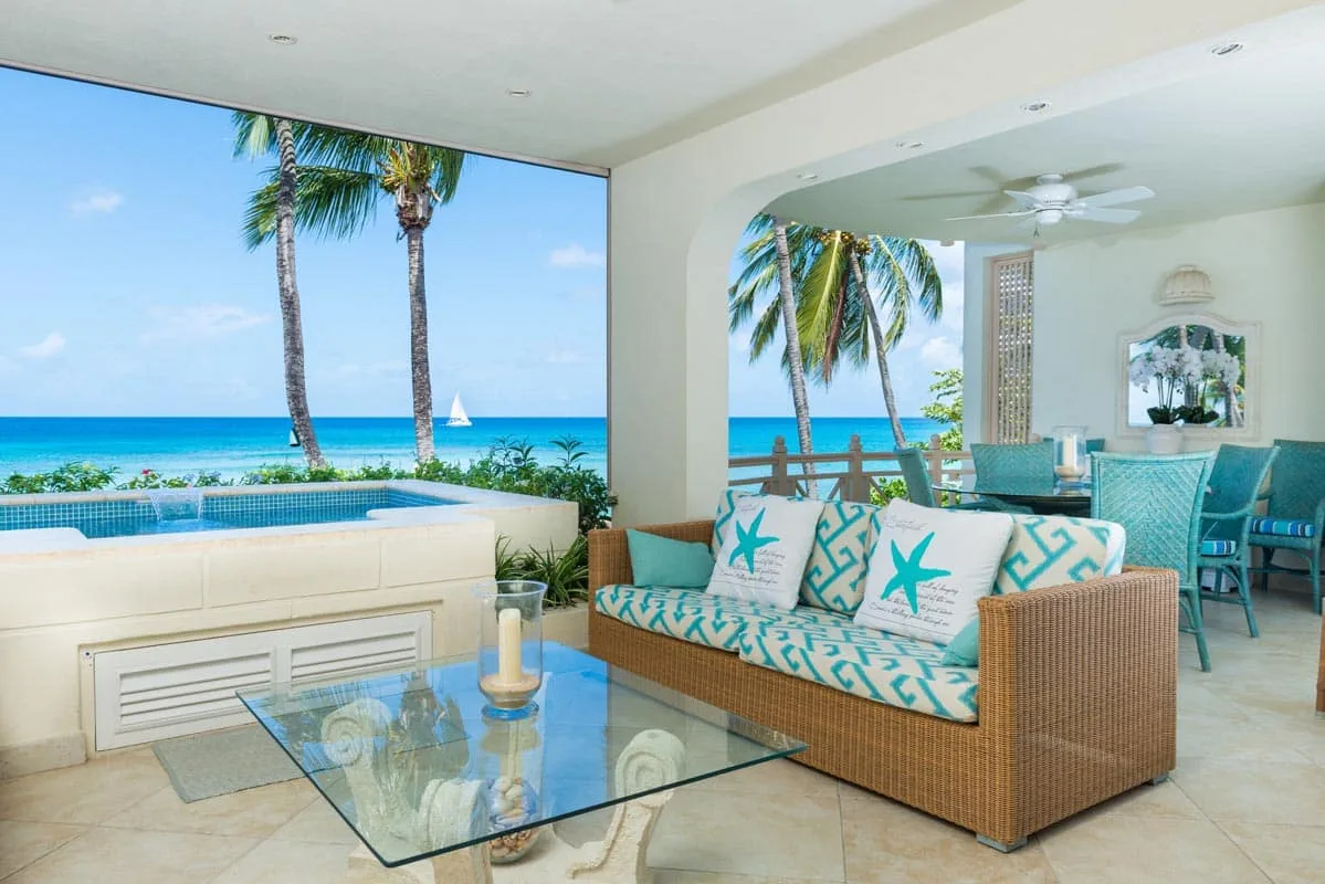 A bright living room opens onto a pool and ocean view, with turquoise-accented seating.