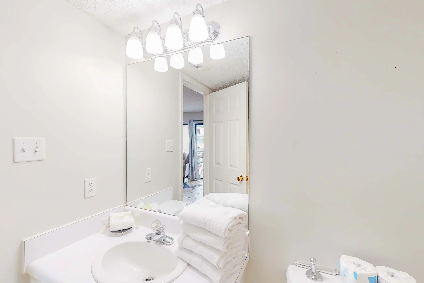 Un tocador de baño luminoso con un espejo grande y toallas dobladas.