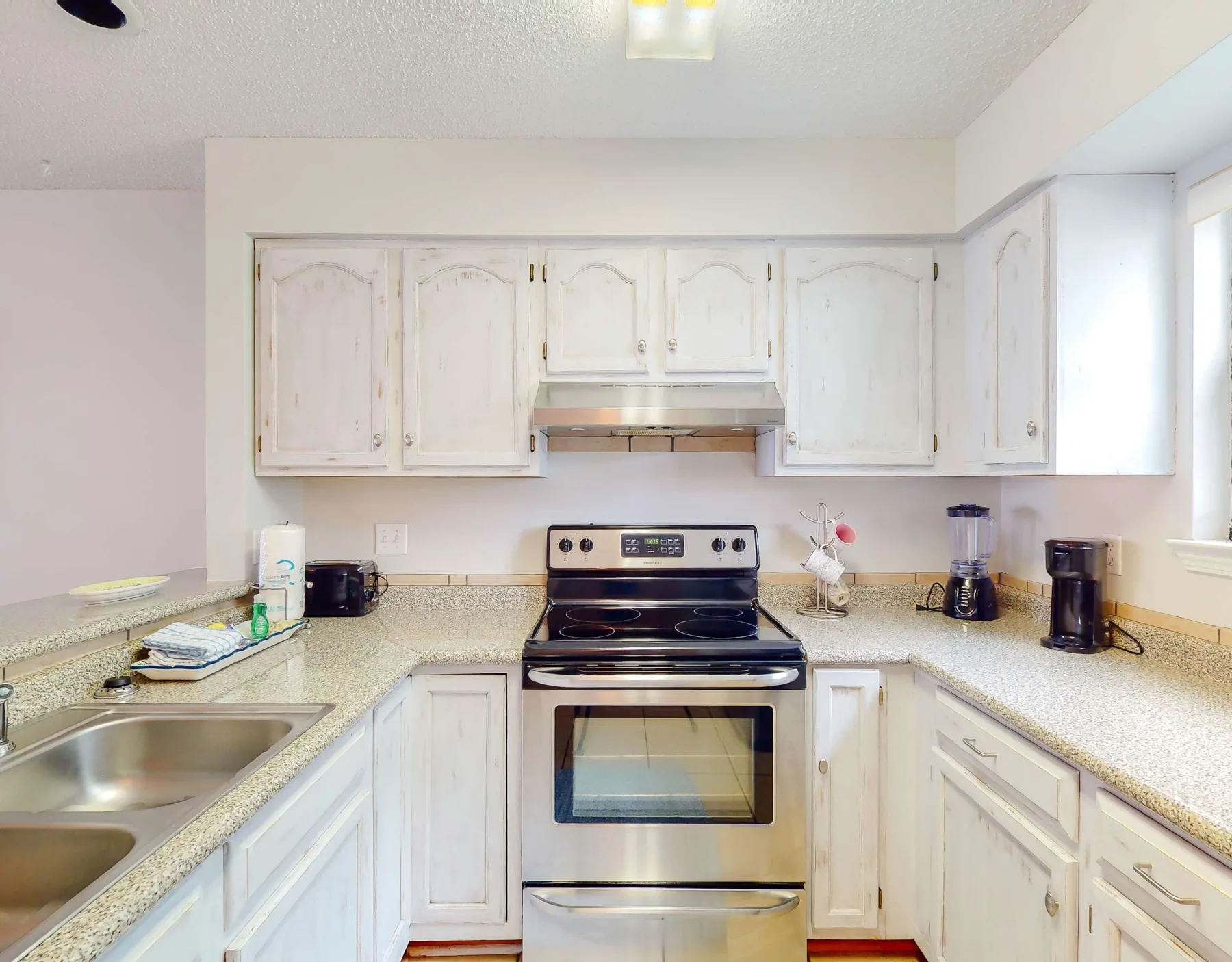 Una cocina luminosa con gabinetes blancos, encimera y una estufa central.