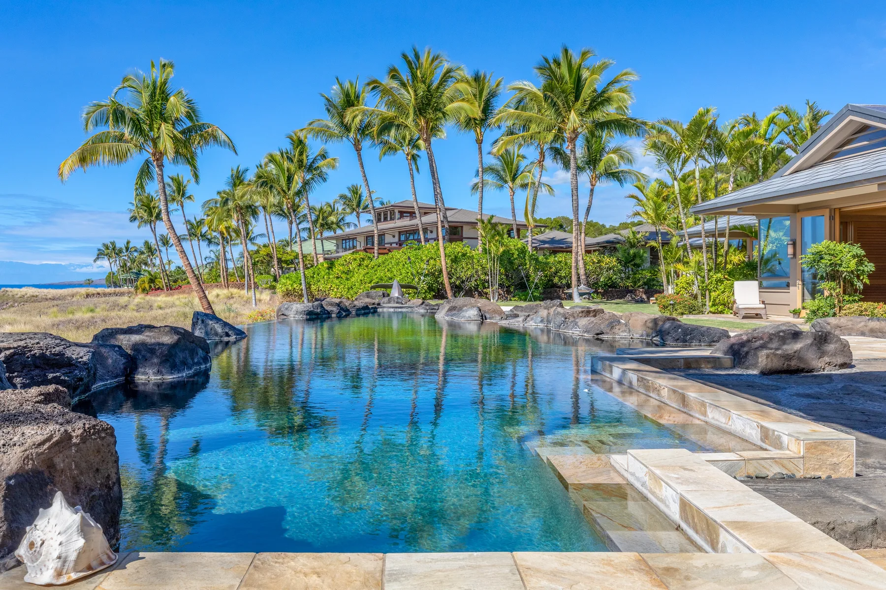 Una piscina tropical rodeada de palmeras y paisajismo de piedra.
