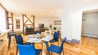 Comedor con una mesa y asientos azules bajo vigas de madera a la vista.