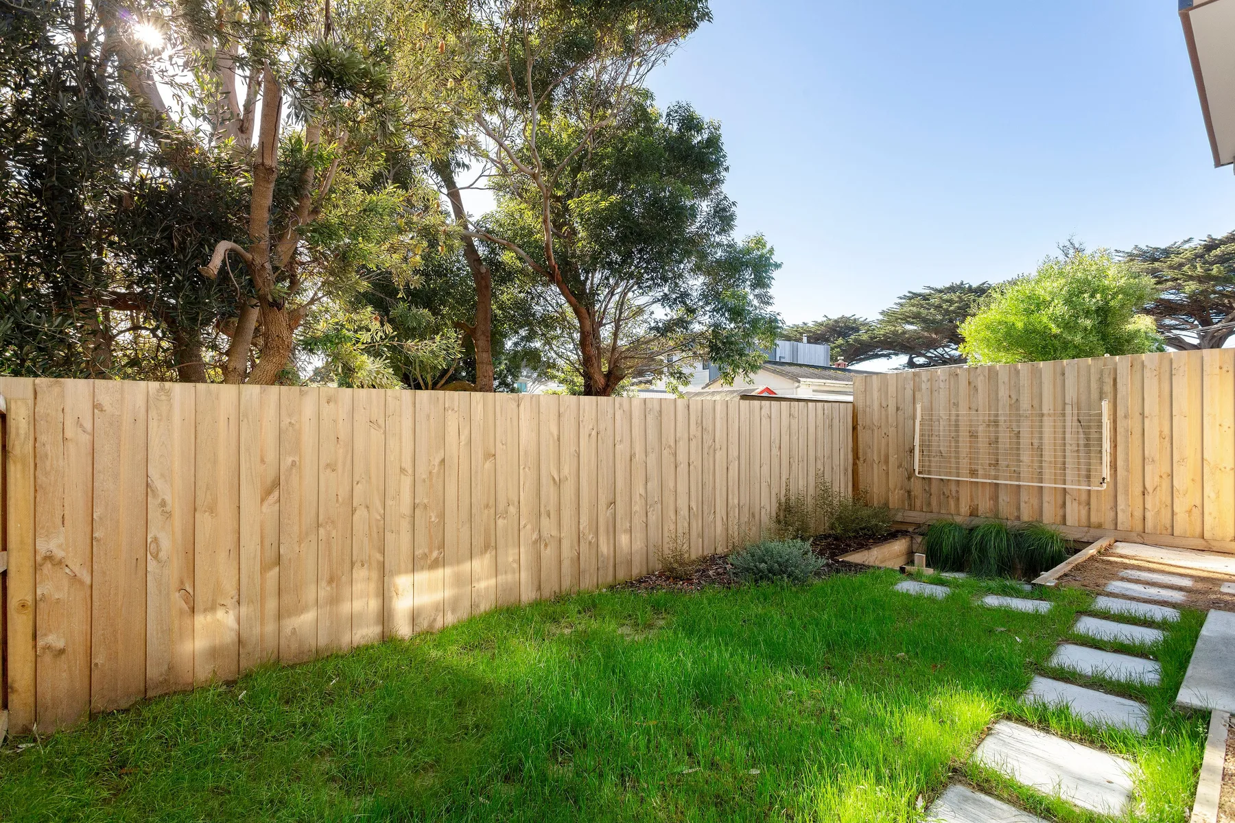 A grassy outdoor yard is enclosed by a wooden fence, with stepping stones along one side.