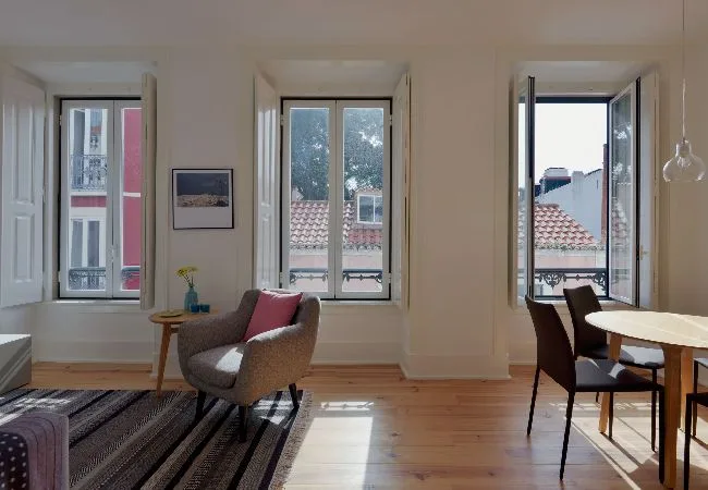 A bright living and dining area has tall windows, seating, and a wooden table.