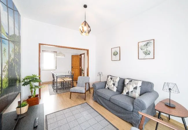 Una sala luminosa con asientos grises y un comedor al fondo.