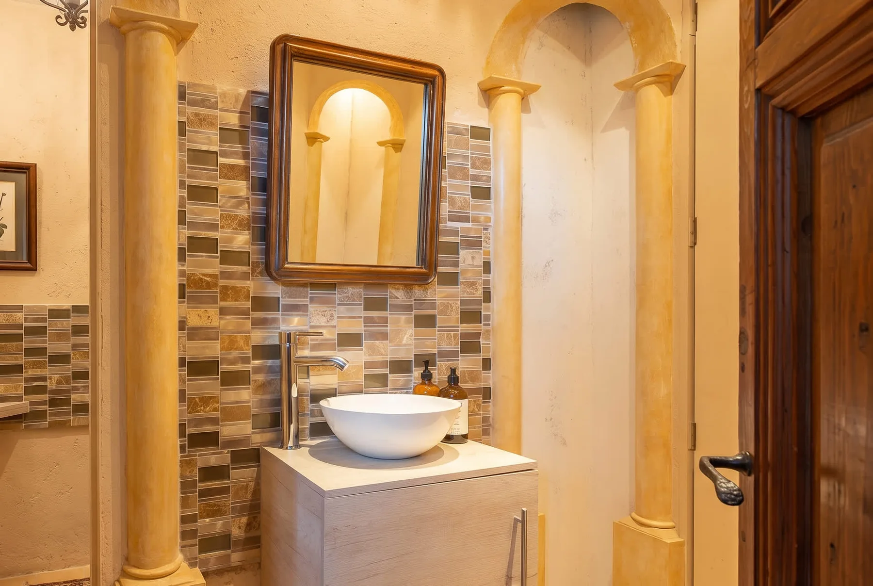 A bathroom vanity with a white basin, tiled wall, and framed mirror.