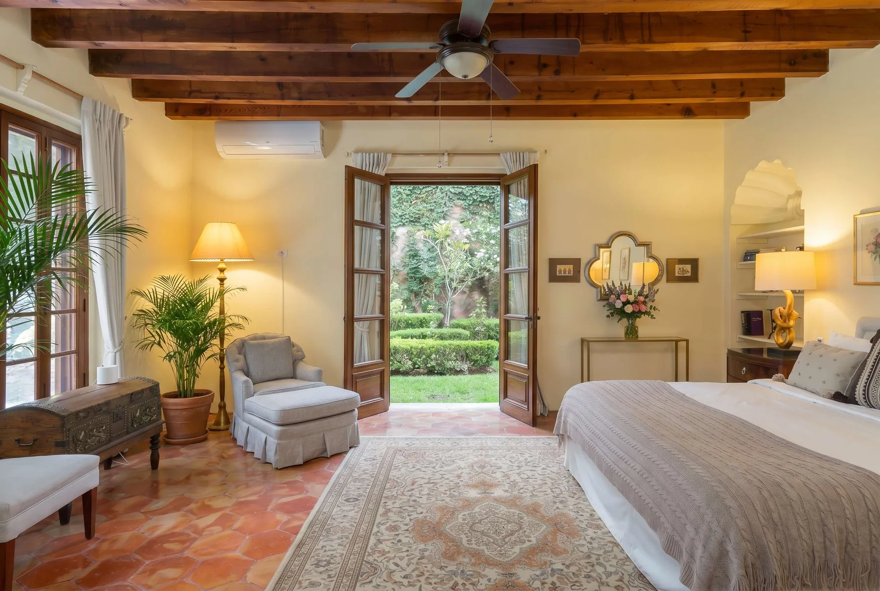 A bedroom with a large bed, seating, and open doors overlooking a garden.