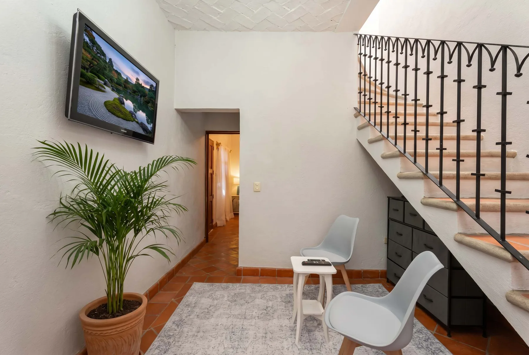 A tiled interior entryway has a staircase, two chairs, and a potted plant.