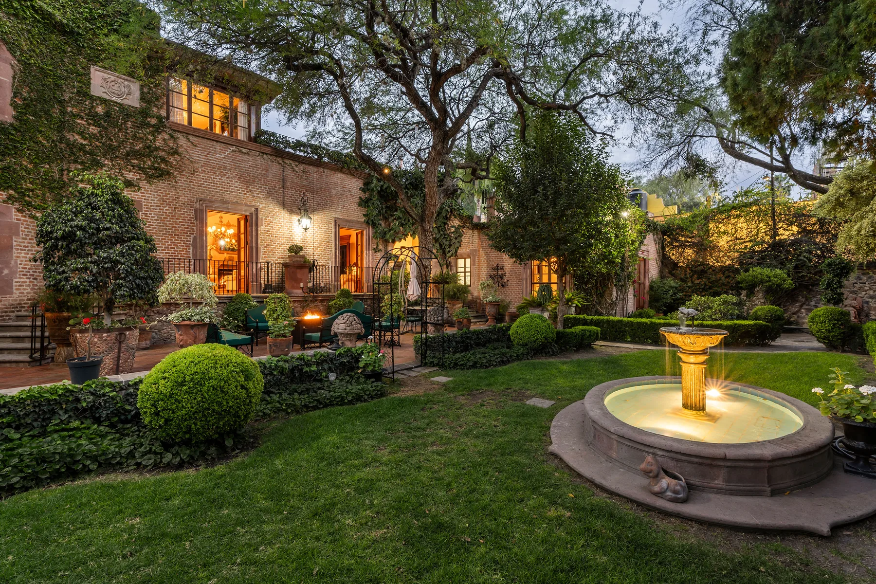 A landscaped courtyard with a lit fountain, greenery, and a brick building.