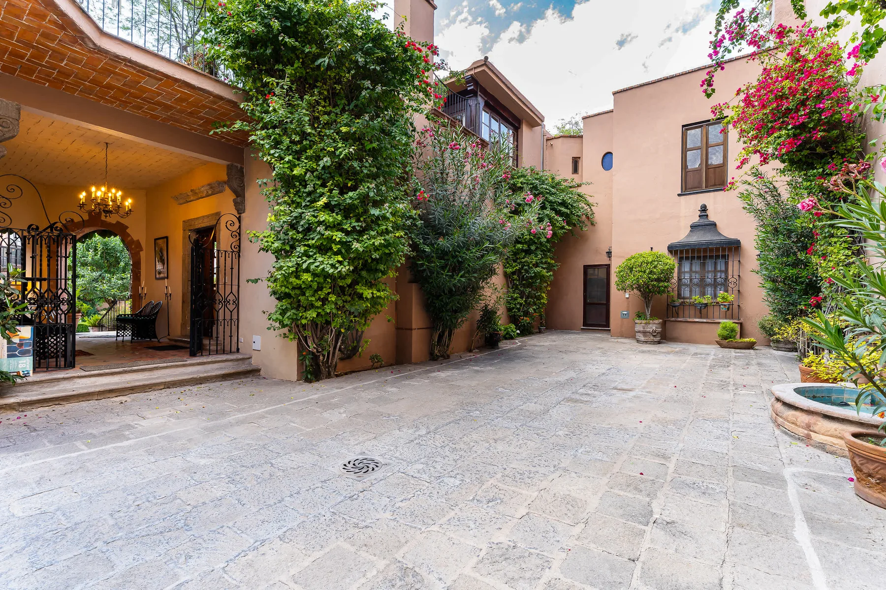 A paved courtyard bordered by peach-colored buildings and leafy flowering plants.