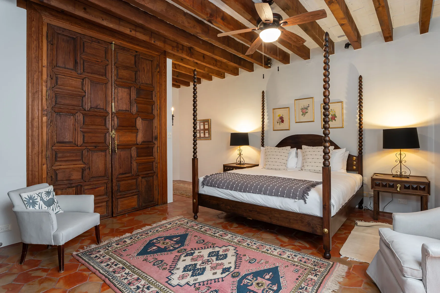 A bedroom with a four-poster bed, wooden ceiling beams, and a patterned rug.