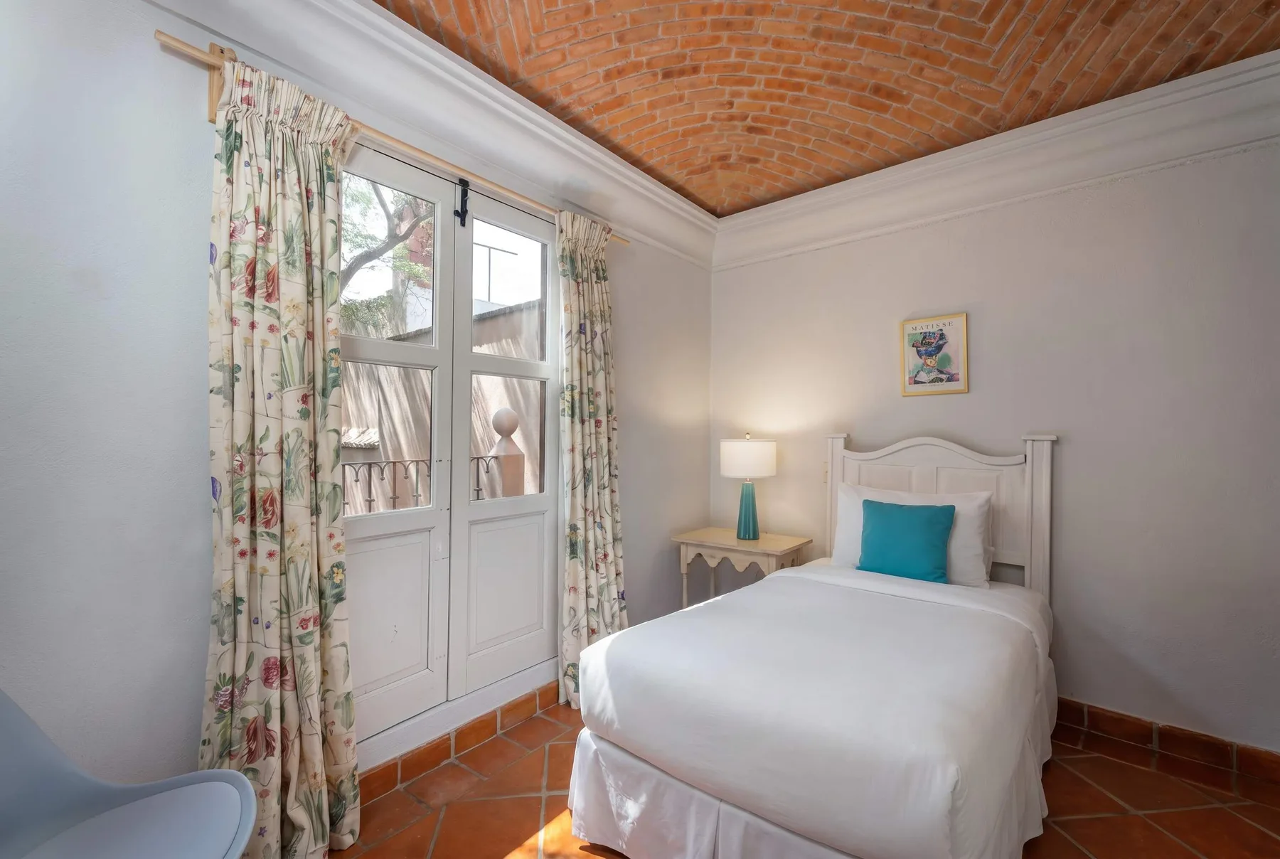 A bedroom with a white bed, patterned curtains, and a brick ceiling.