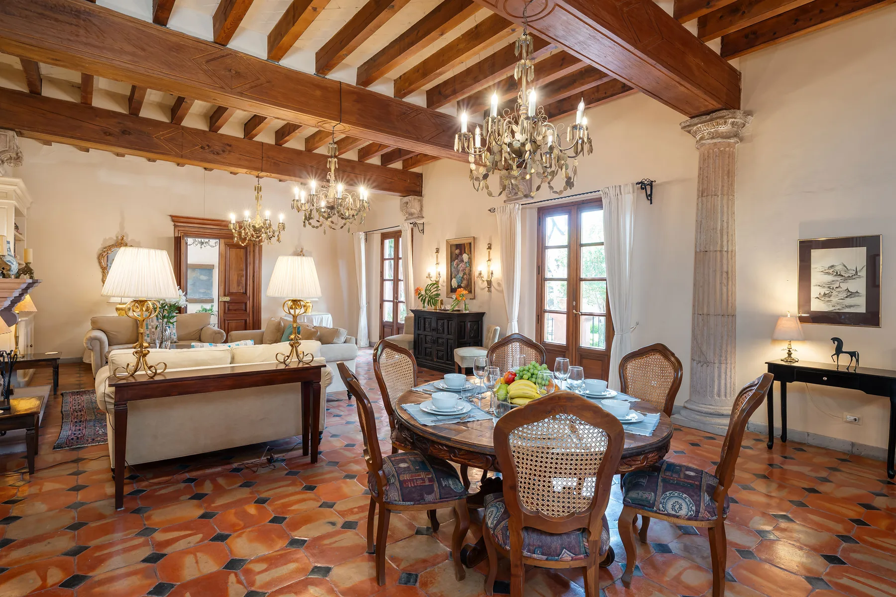 A dining room with a set table, seating, and exposed wooden ceiling beams.