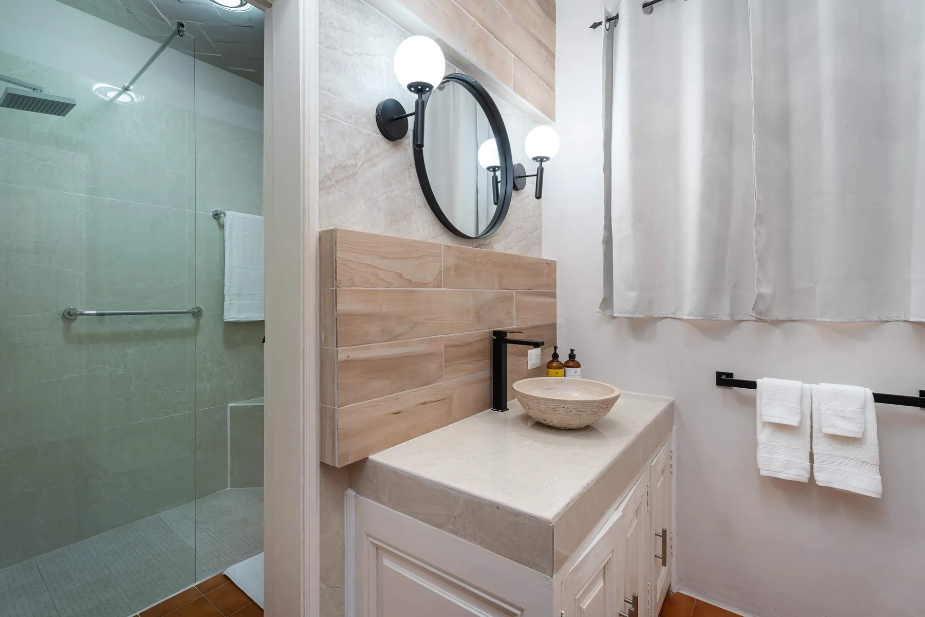 A bathroom vanity with a vessel sink sits beside a glass shower.