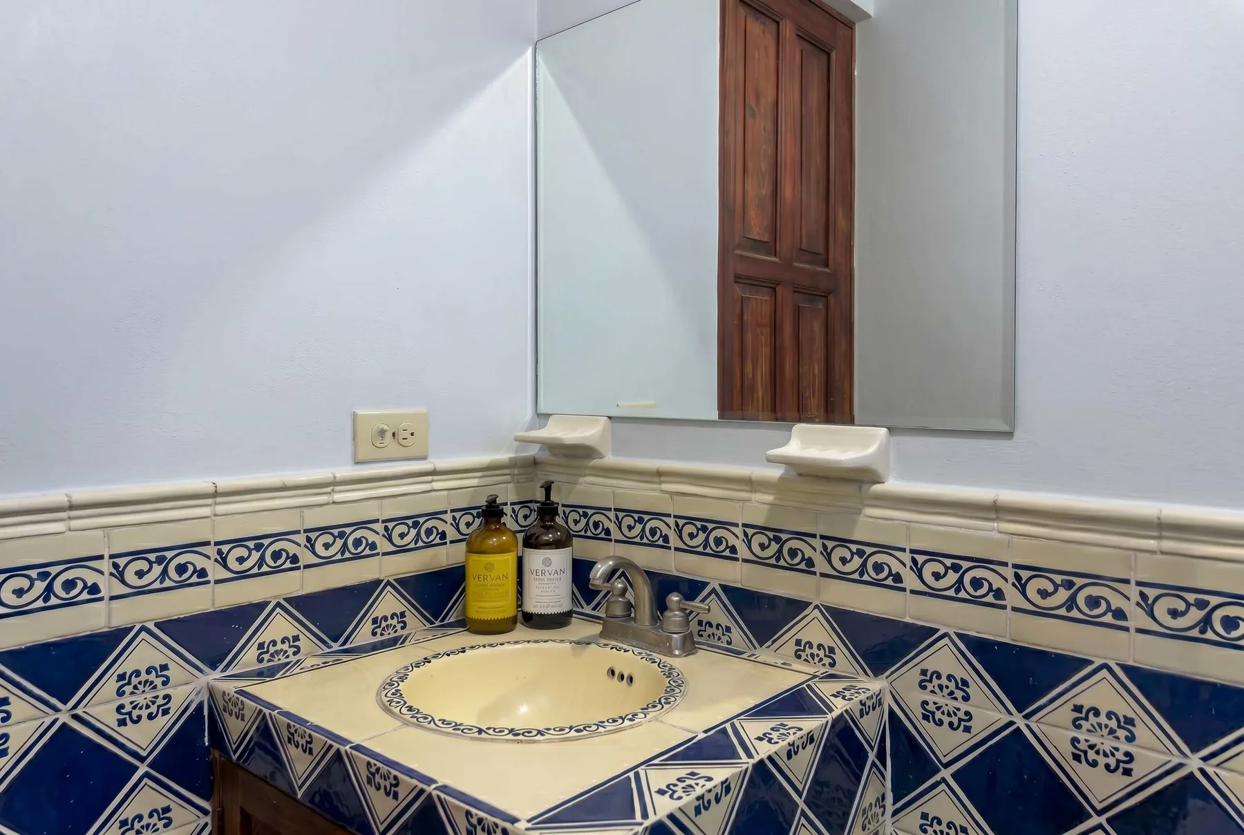 A tiled bathroom vanity with a sink, faucet, and wall mirror.