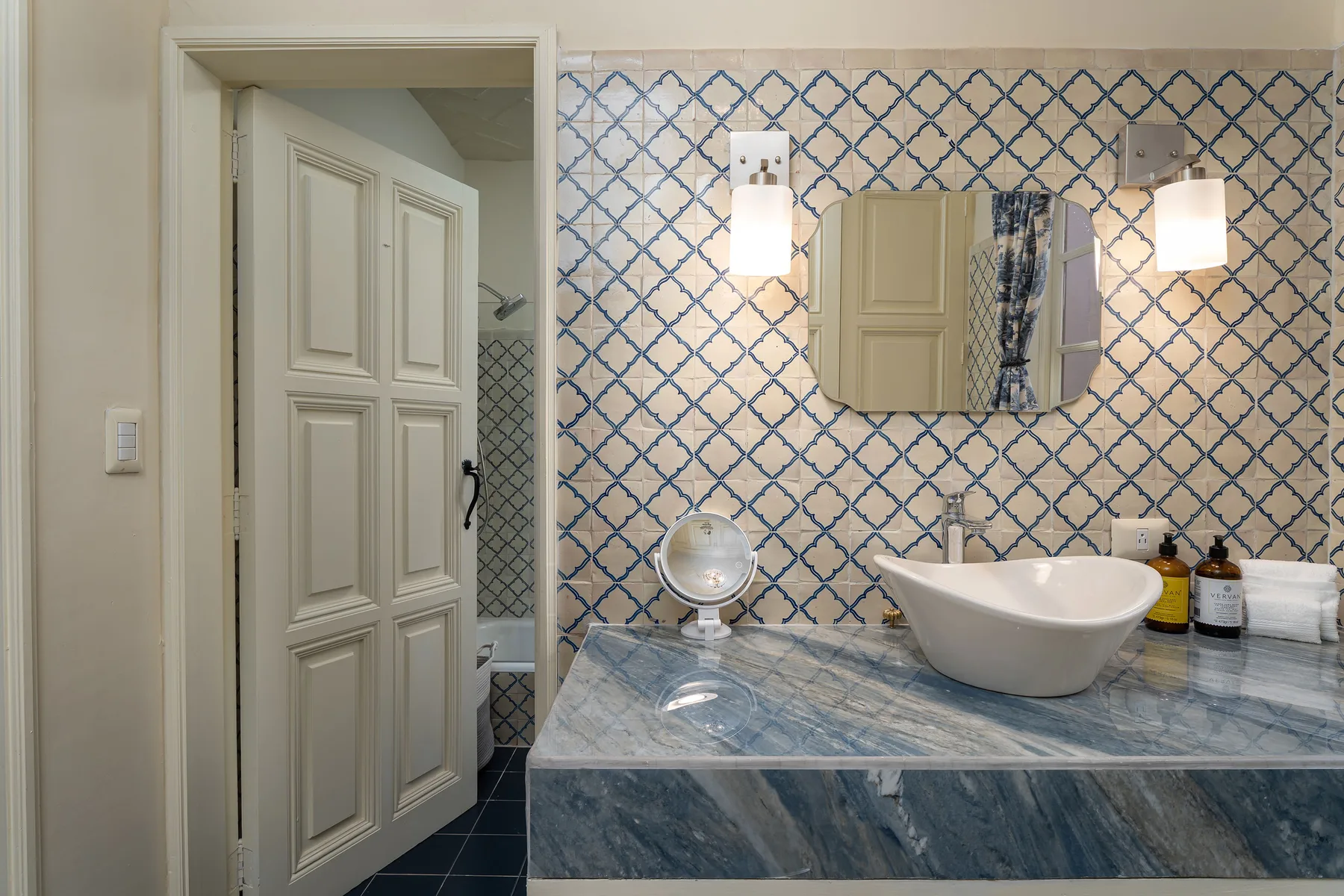 A bathroom vanity with a vessel sink and patterned tile walls.
