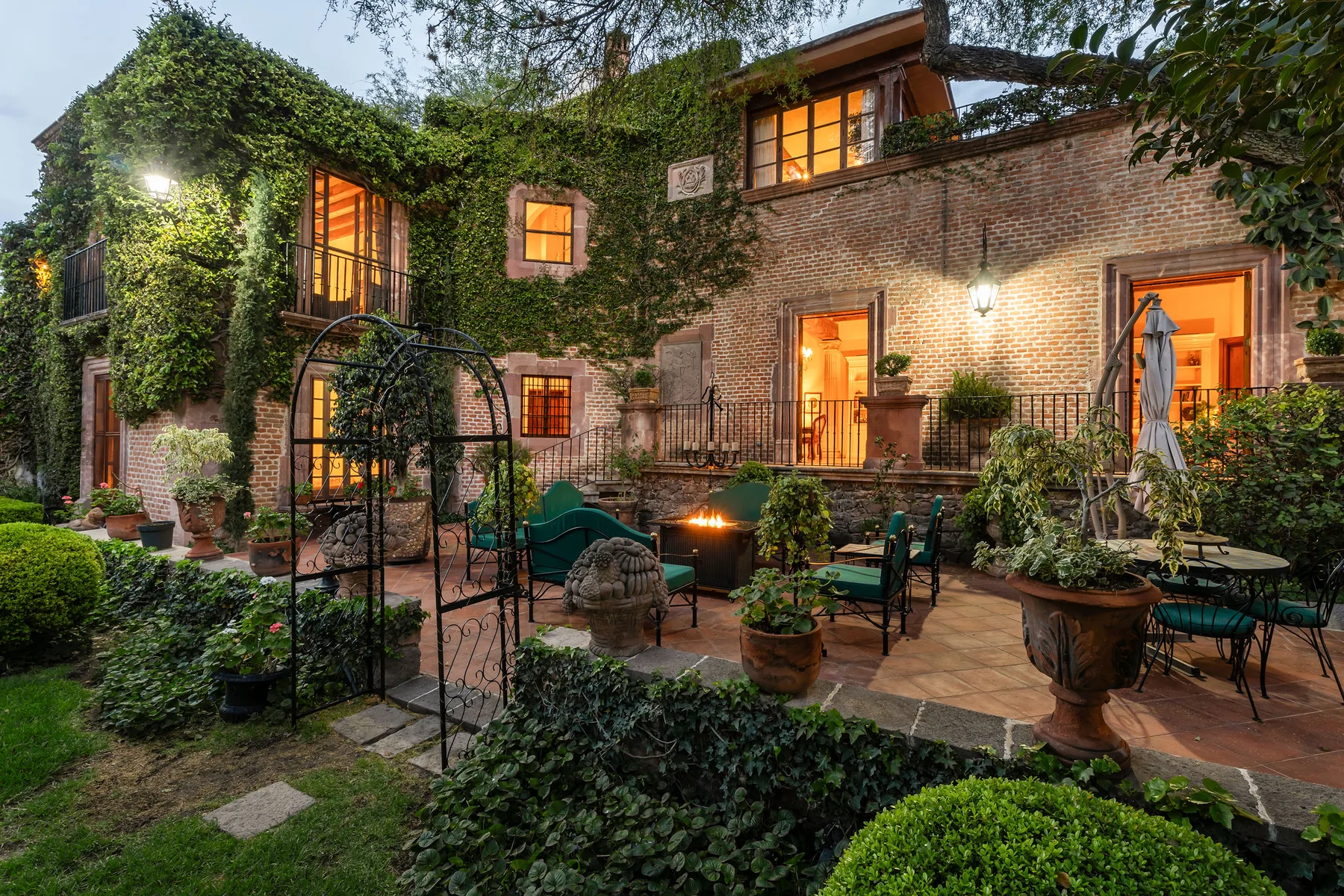 A brick building opens onto a garden patio with outdoor seating and plants.