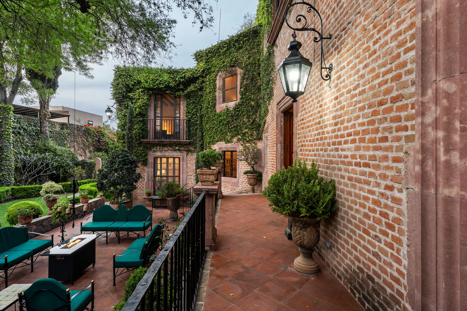 A brick courtyard patio with outdoor seating, potted plants, and climbing greenery.