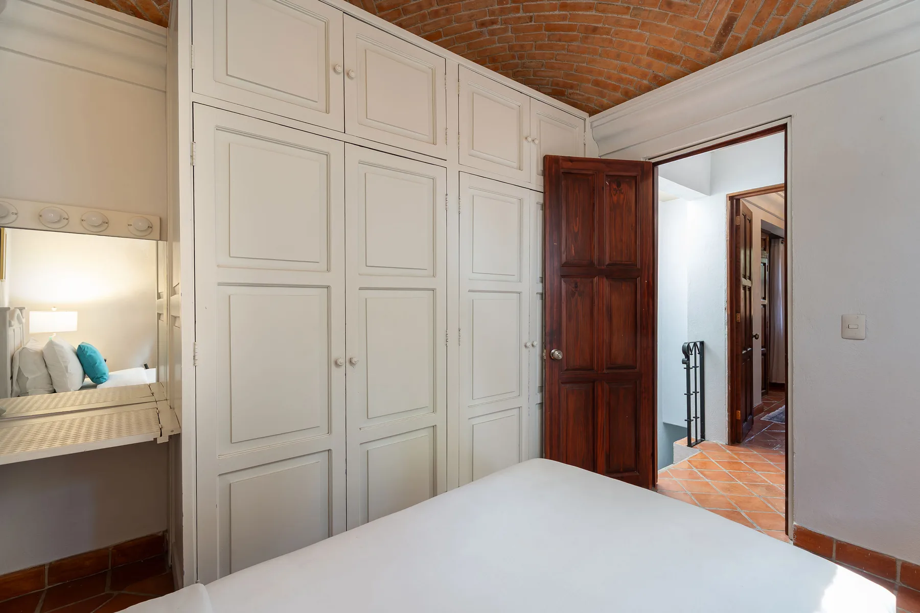 A bedroom with built-in white cabinets, a bed, and an open wooden door.