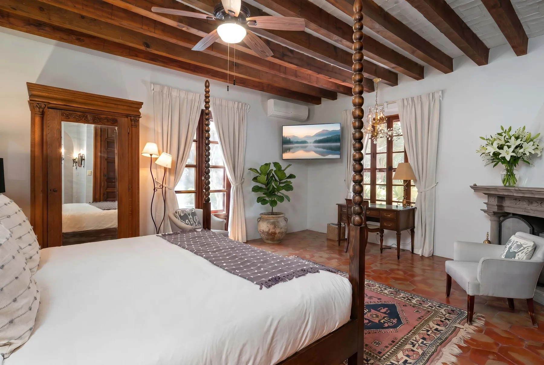 A bedroom with a large bed, exposed wooden ceiling beams, and a seating area.
