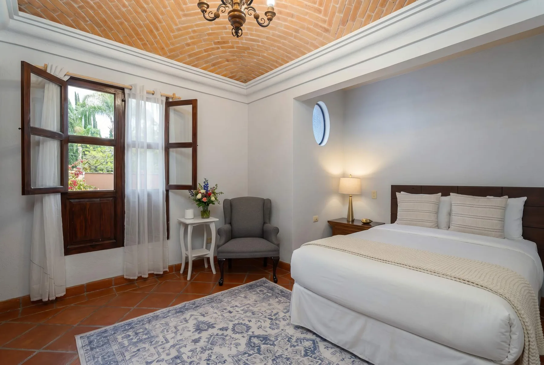 A bedroom with a bed, an armchair, and an open window.