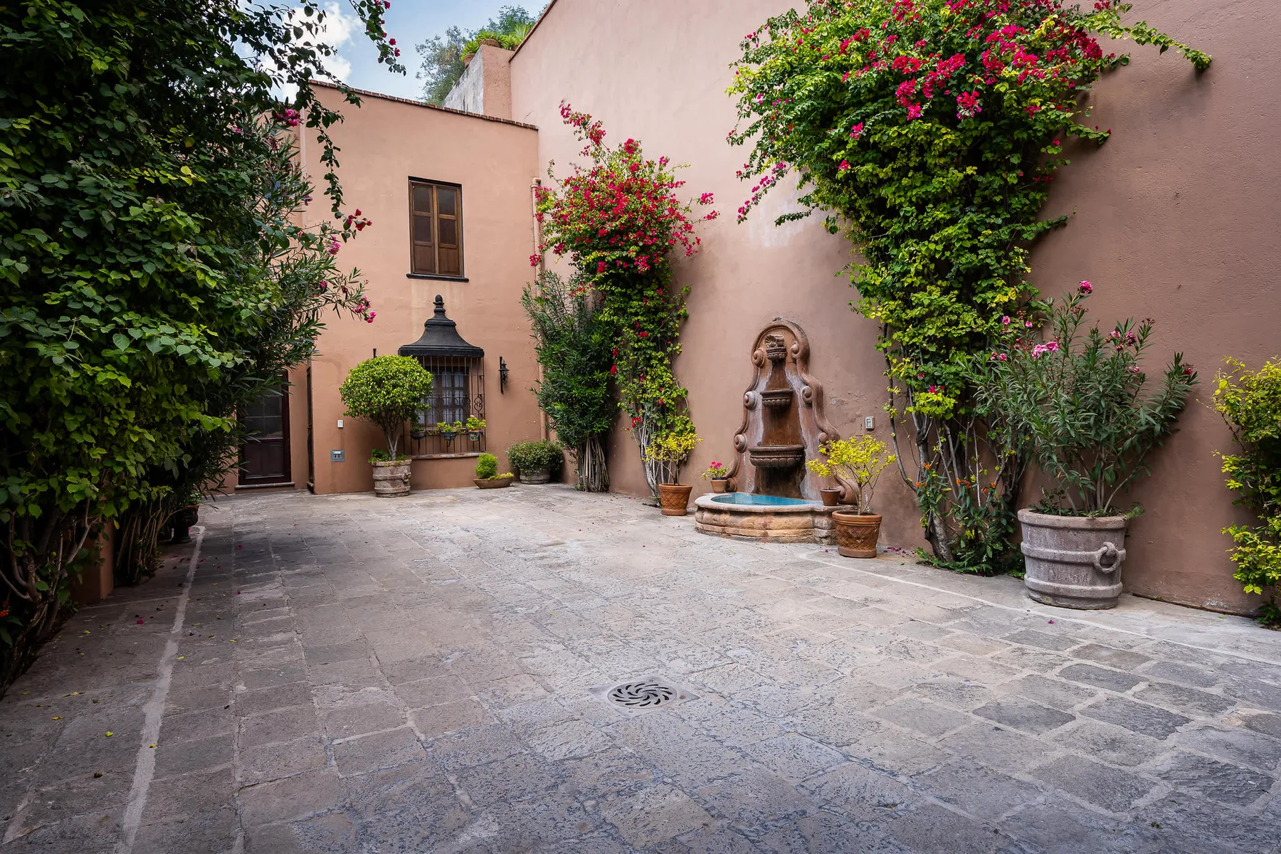 A paved courtyard features a small fountain and flowering vines along the walls.