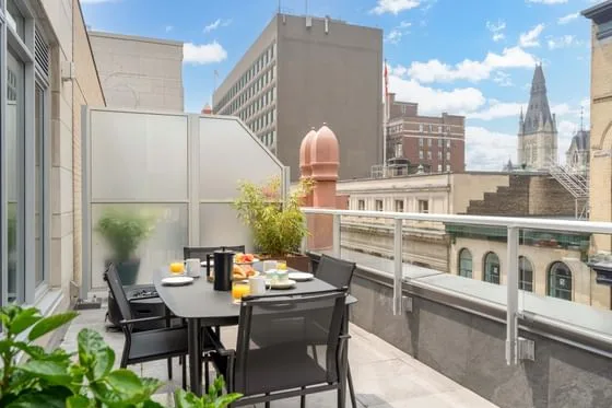 Espacio representativo del hotel: Terraza al aire libre con una mesa de comedor y edificios de la ciudad al fondo.