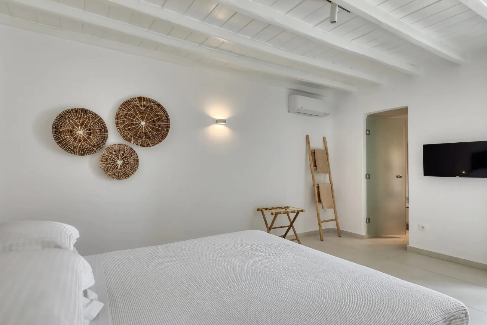 A bright bedroom with a bed, woven wall decorations, and a wall-mounted television.