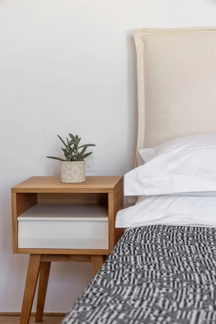 A bedroom corner with a bed, patterned bedding, and a wooden bedside table.
